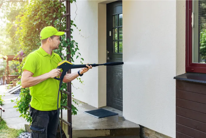 A professional pressure washing the side of a house with rendered walls